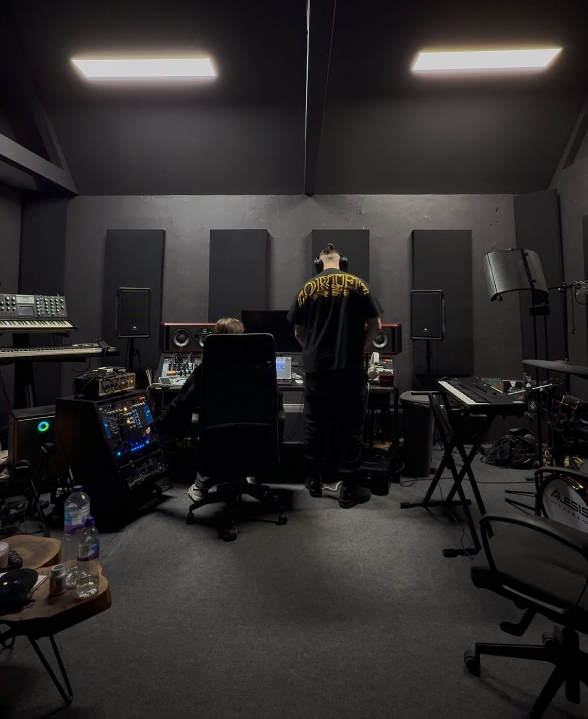 MNEEMO (Yaroslav Gorovoy) & FLASH (Anton Ditiashov): one is sitting at a computer, the other is standing in headphones. Dark surroundings, music equipment, relaxed atmosphere.