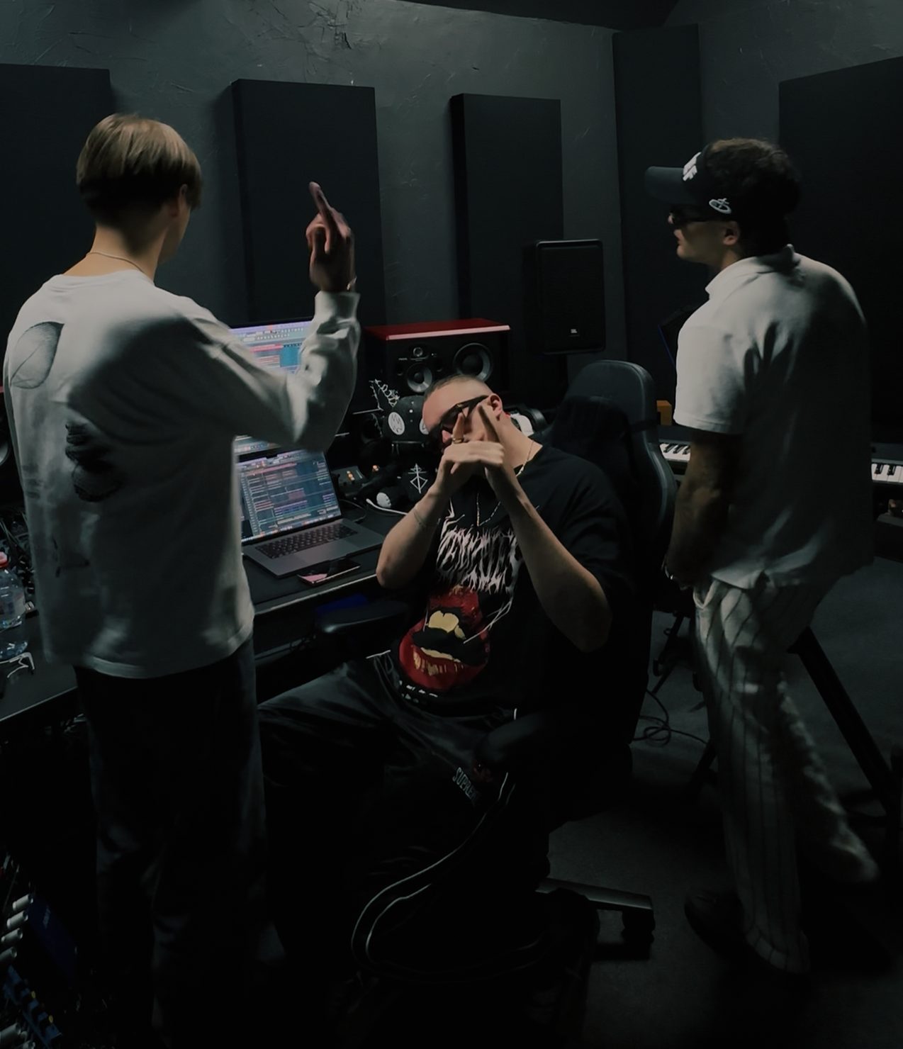 MNEEMO (Yaroslav Gorovoy), FLASH (Anton Ditiashov) & E4TEEN in a recording studio: one is sitting at the mixing desk while the others stand nearby. Dark setting, with software visible on the monitor.