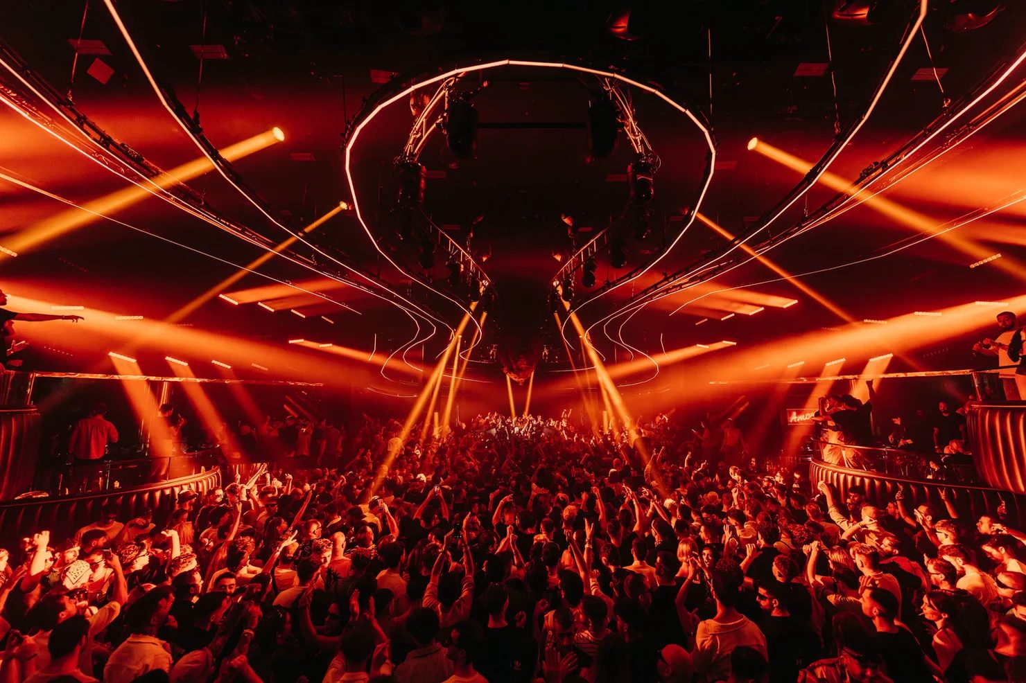 Crowd with hands up under orange lasers at an Ibiza big-room club night