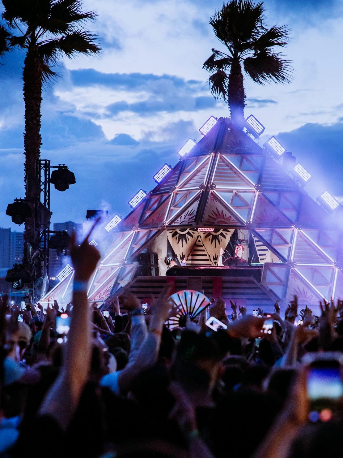 DnB Allstars outdoor festival stage with pyramid production, palm trees, lights and crowd atmosphere
