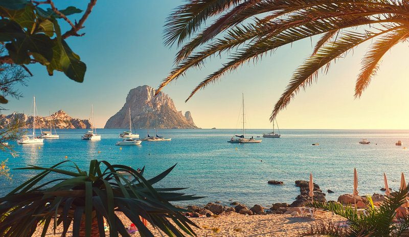 Ibiza coastline with Es Vedra rock seen through palm fronds, home to the island superclubs