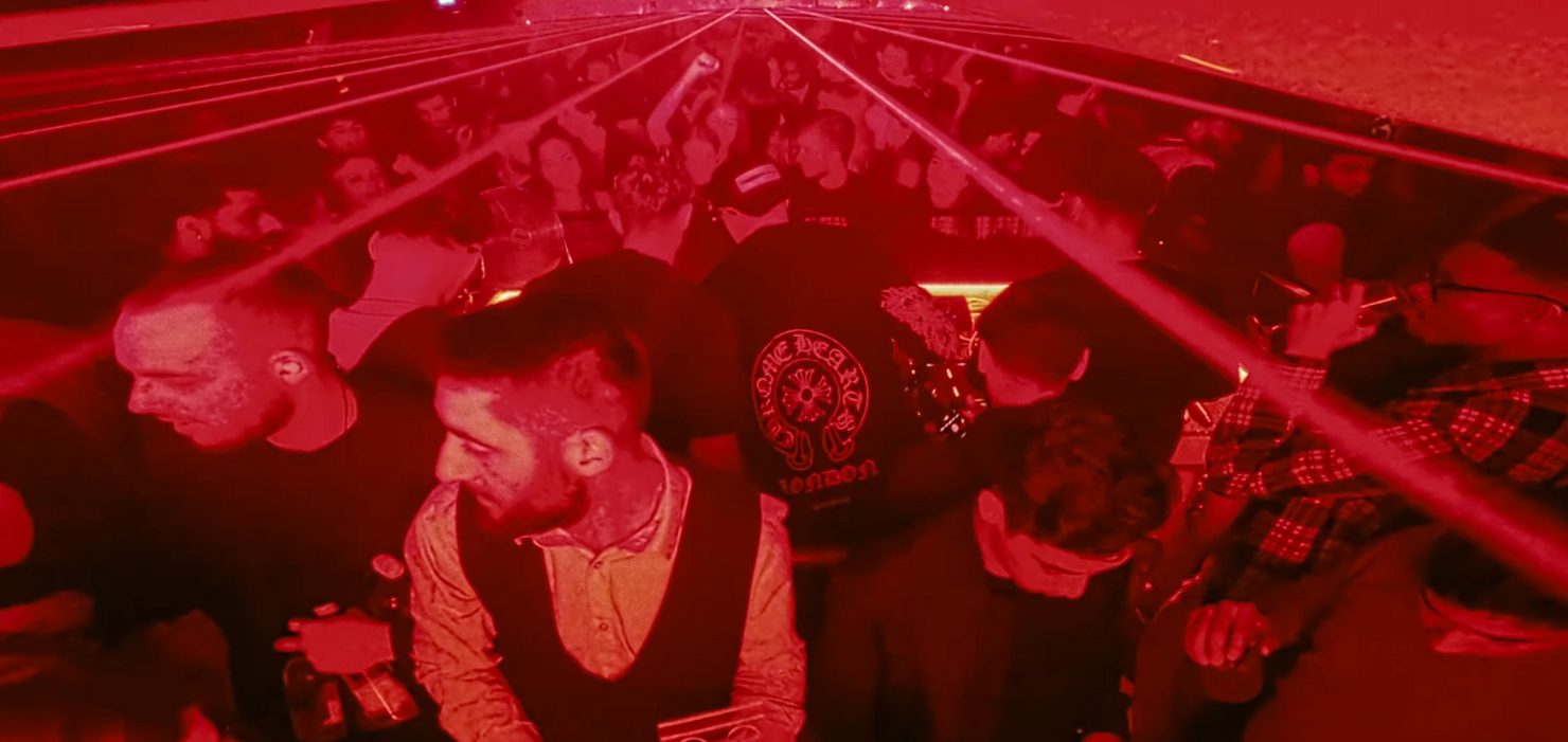 Crowded nightclub scene with red lighting, people dancing, and drinks in hand. Lasers cross the room, creating an energetic atmosphere. MNEEMO (Yaroslav Gorovoy) DJing in the middle.