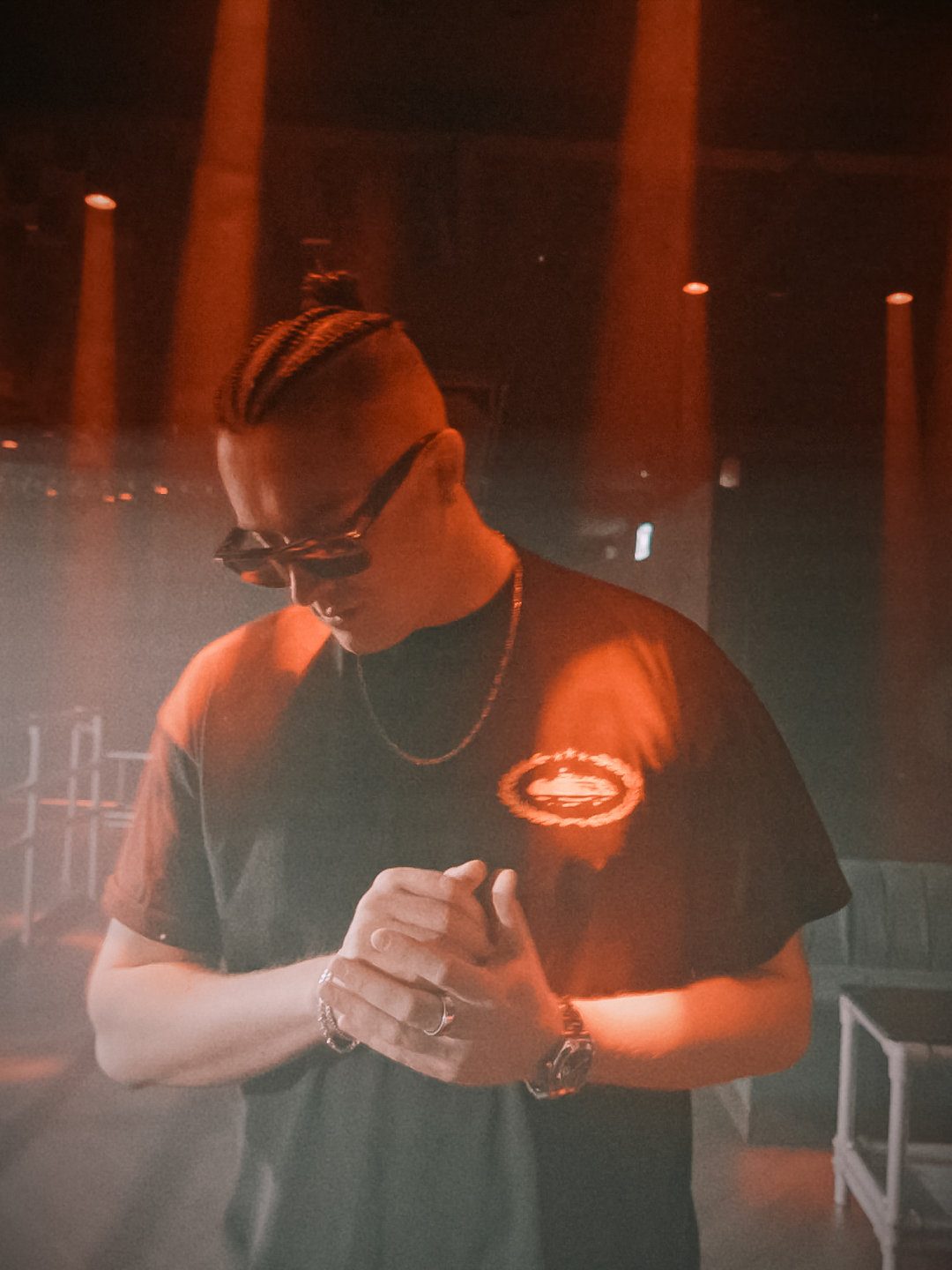 MNEEMO (Yaroslav Gorovoy) wearing dark glasses and a black T-shirt, standing in a club under red lighting. He has a chain, with his arms folded and a calm mood.