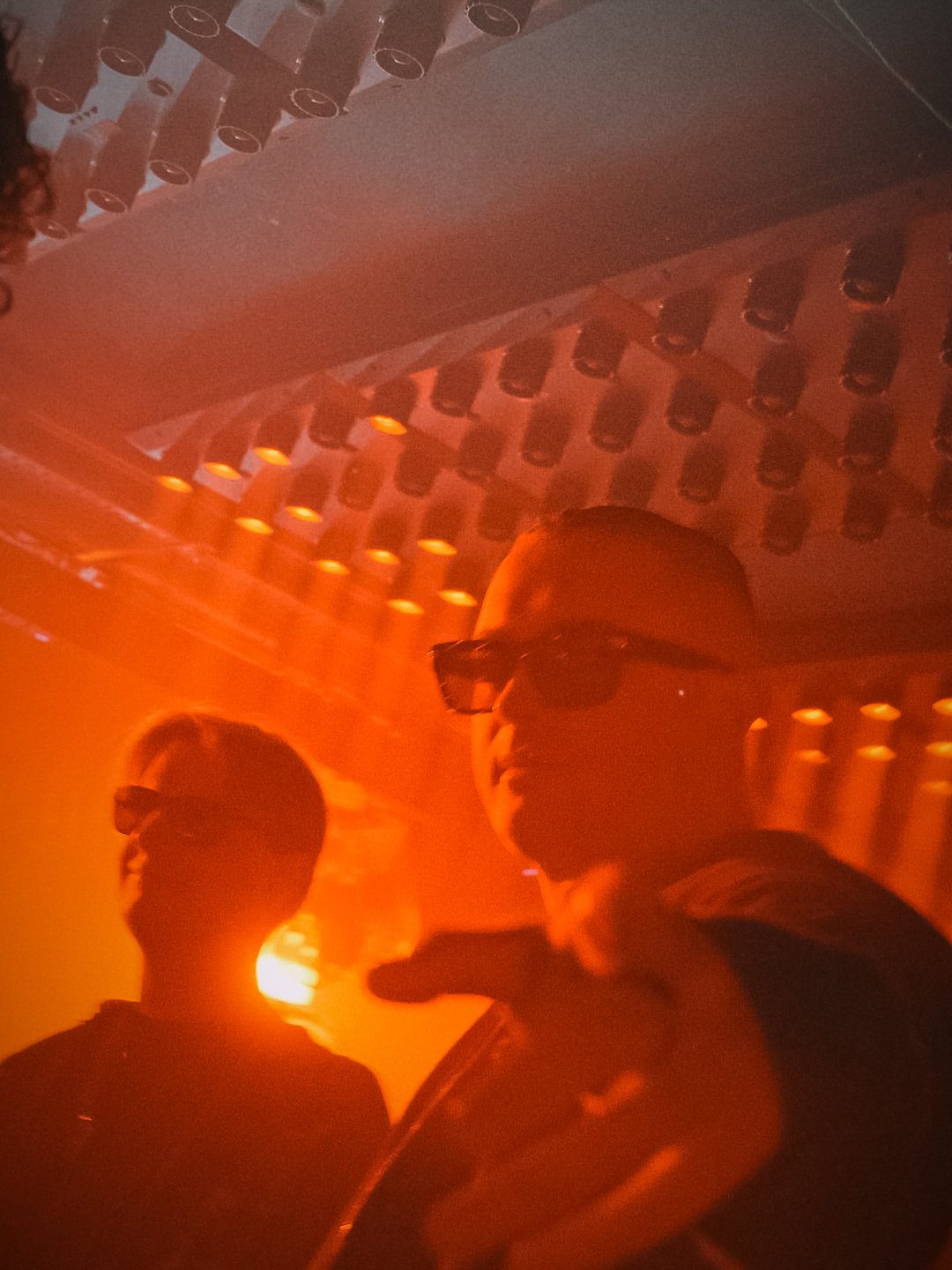 MNEEMO (Yaroslav Gorovoy) & FLASH wearing sunglasses in a club with orange lighting. One of them is pointing with his hand. The ceiling is lit with lamps. Energetic atmosphere.