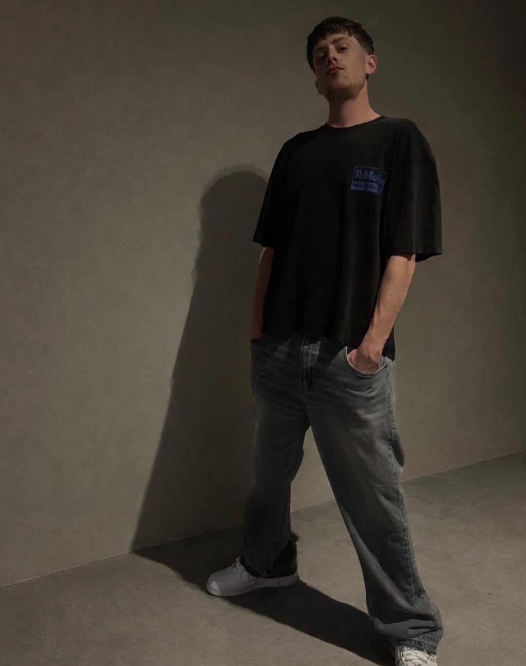 Tom Did It in a black T-shirt and jeans, studio portrait against a plain wall.