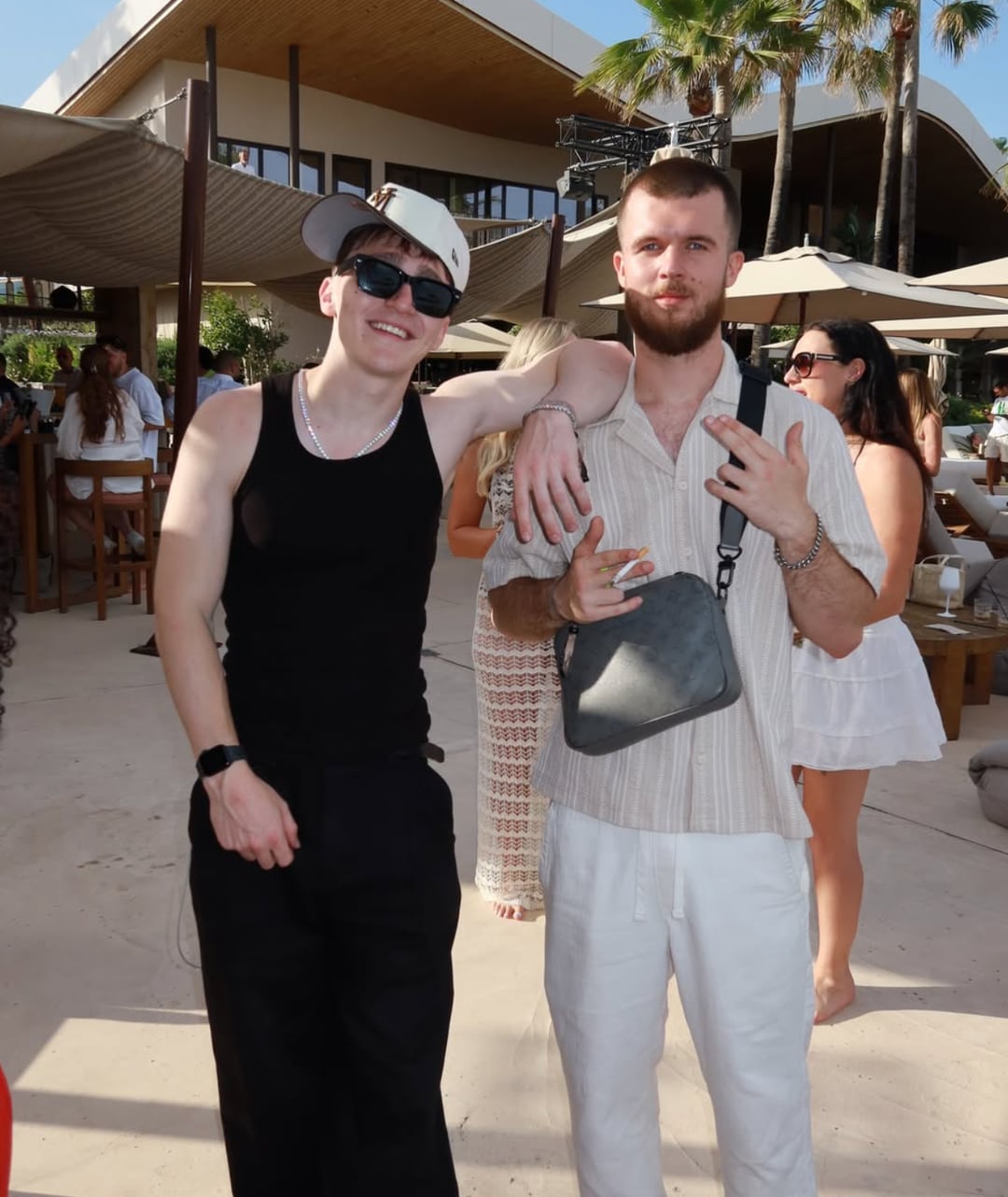 GW and X10 of MORELIFE side by side at a daytime beach club party, palm trees and parasols behind them.