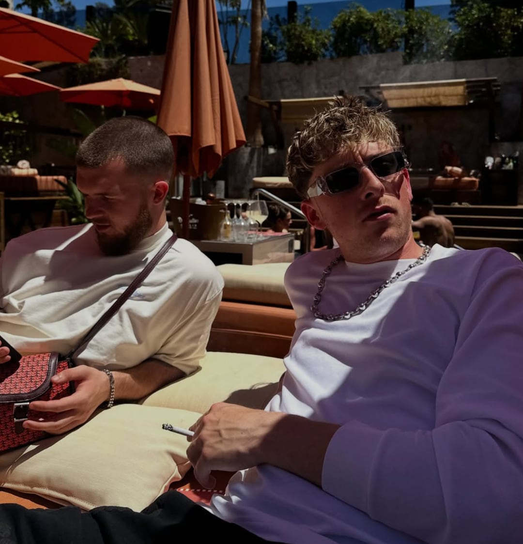 Tom Did It and X10 on sunloungers at a day party, sunglasses on, crowd behind them.