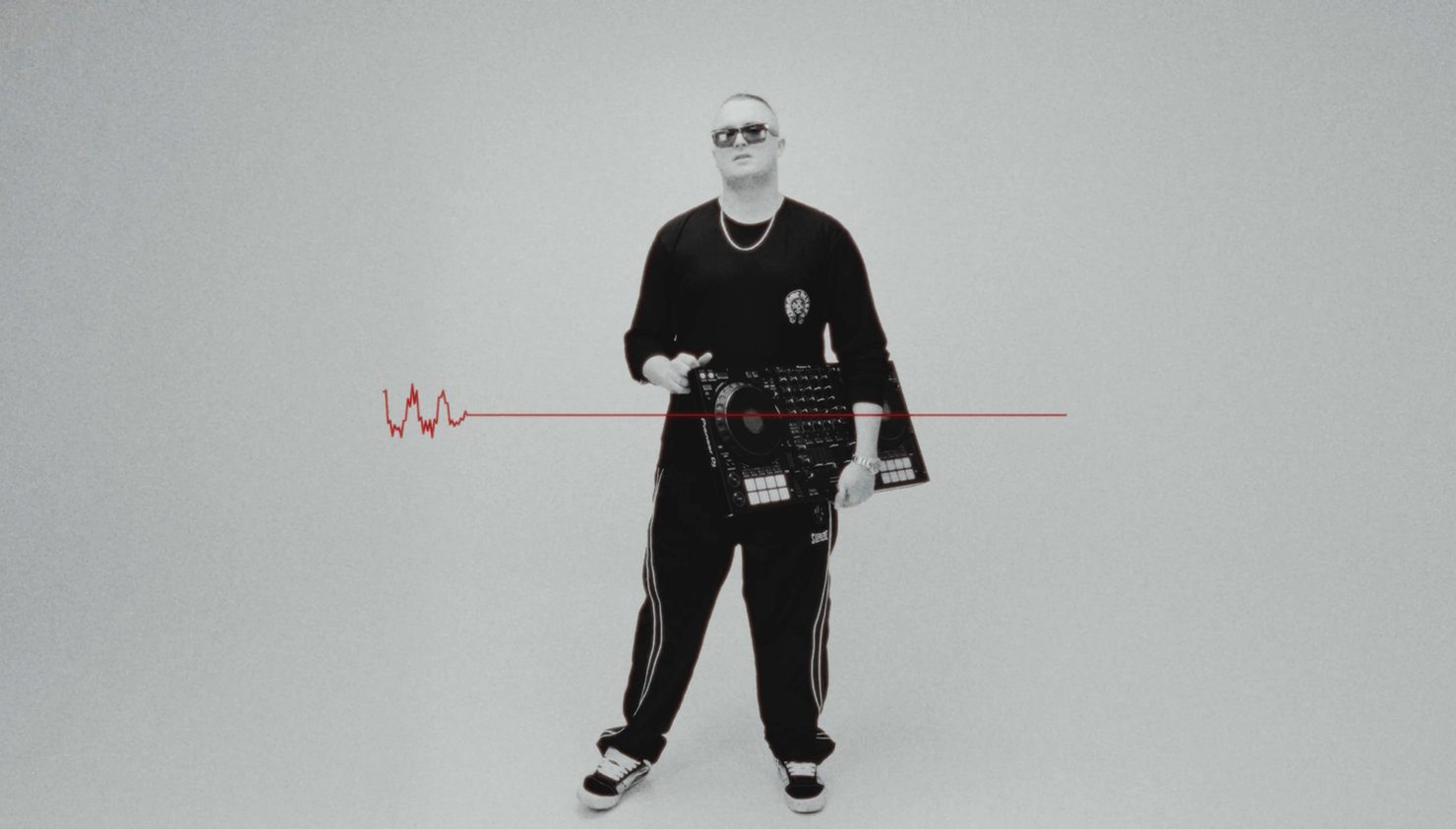 MNEEMO (Yaroslav Gorovoy) in black clothing and sunglasses, holding a DJ mixer. Grey lighting in the background, with a red line running across the image.