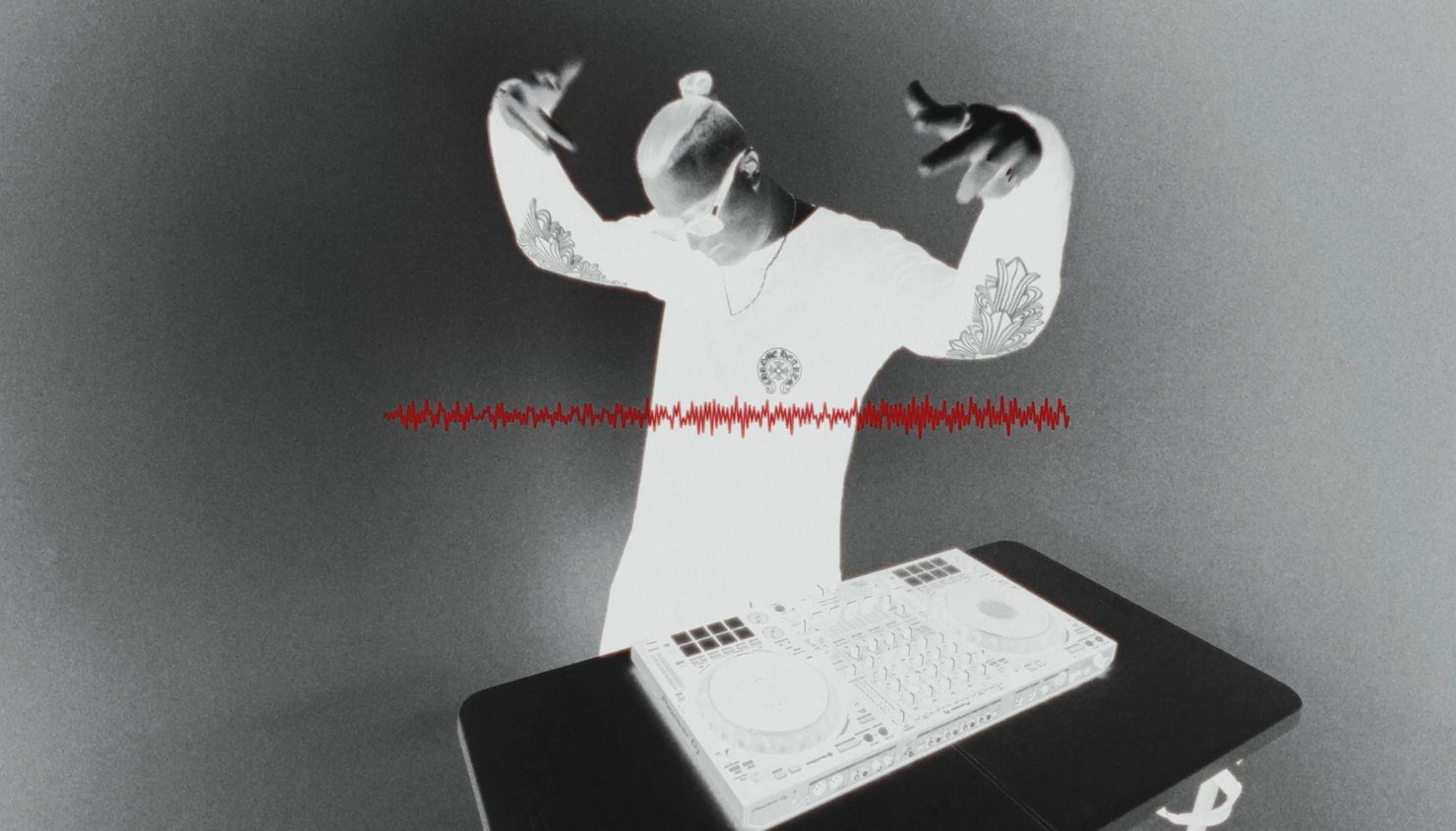 MNEEMO (Yaroslav Gorovoy) wearing headphones, with tattoos on his arms, performing behind the decks. Grey negative-style background with a red sound wave.