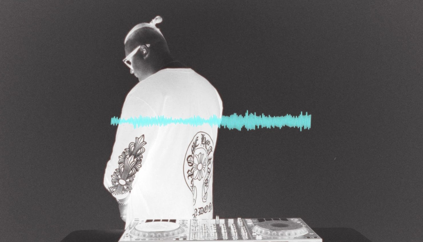 DJ MNEEMO (Yaroslav Gorovoy) wearing headphones, standing at the decks against a black background. A blue sound spectrogram runs across the image. A graphic Chrome Hearts print is visible on the T-shirt.