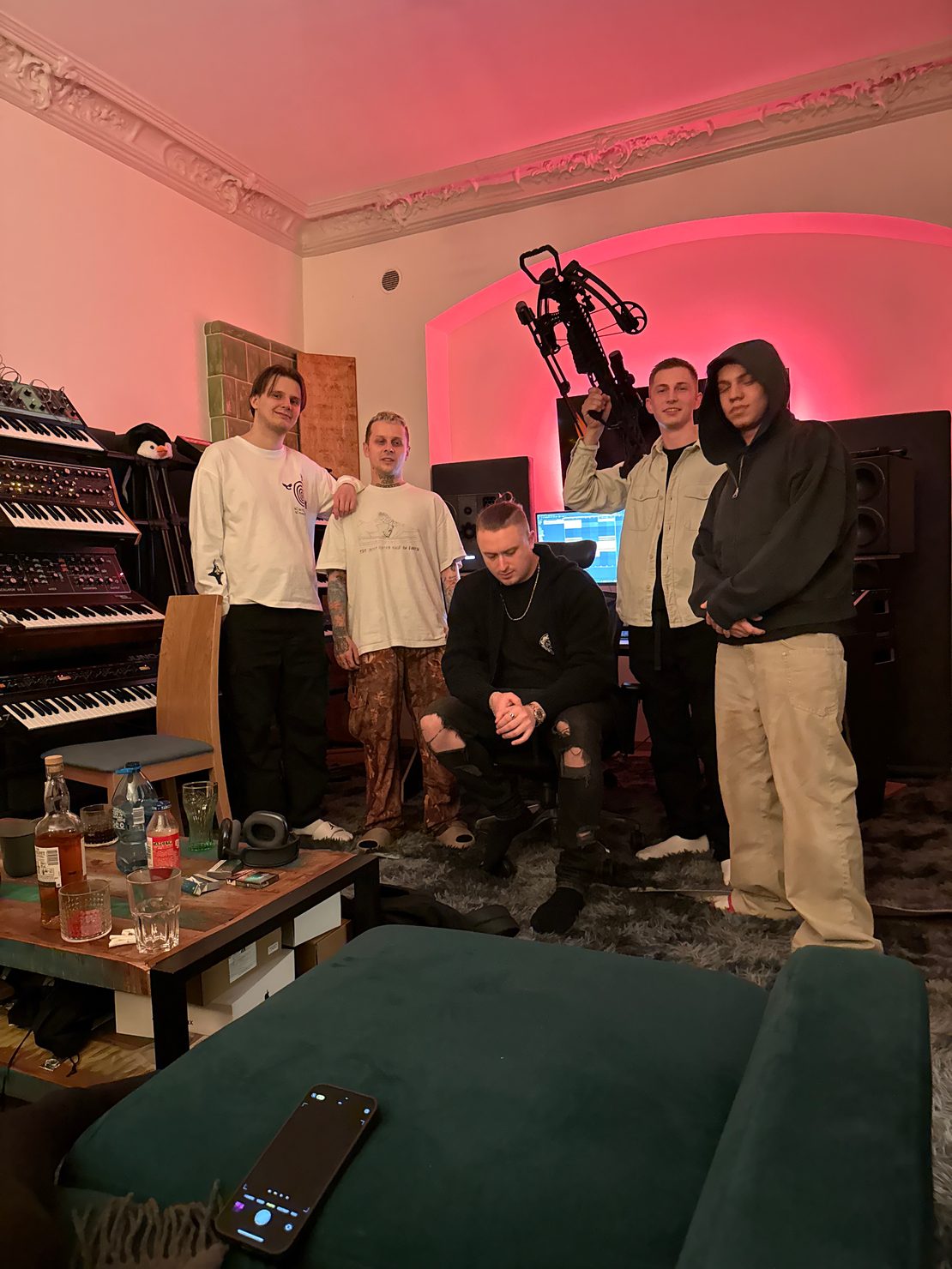 MNEEMO (Yaroslav Gorovoy), FLASH, NIKITAIDISUYDA, SLAVKO and DANIEL OKARO in a music studio with keyboards. One is holding an Arbalet, the background is lit with red light, and there are drinks on the table.