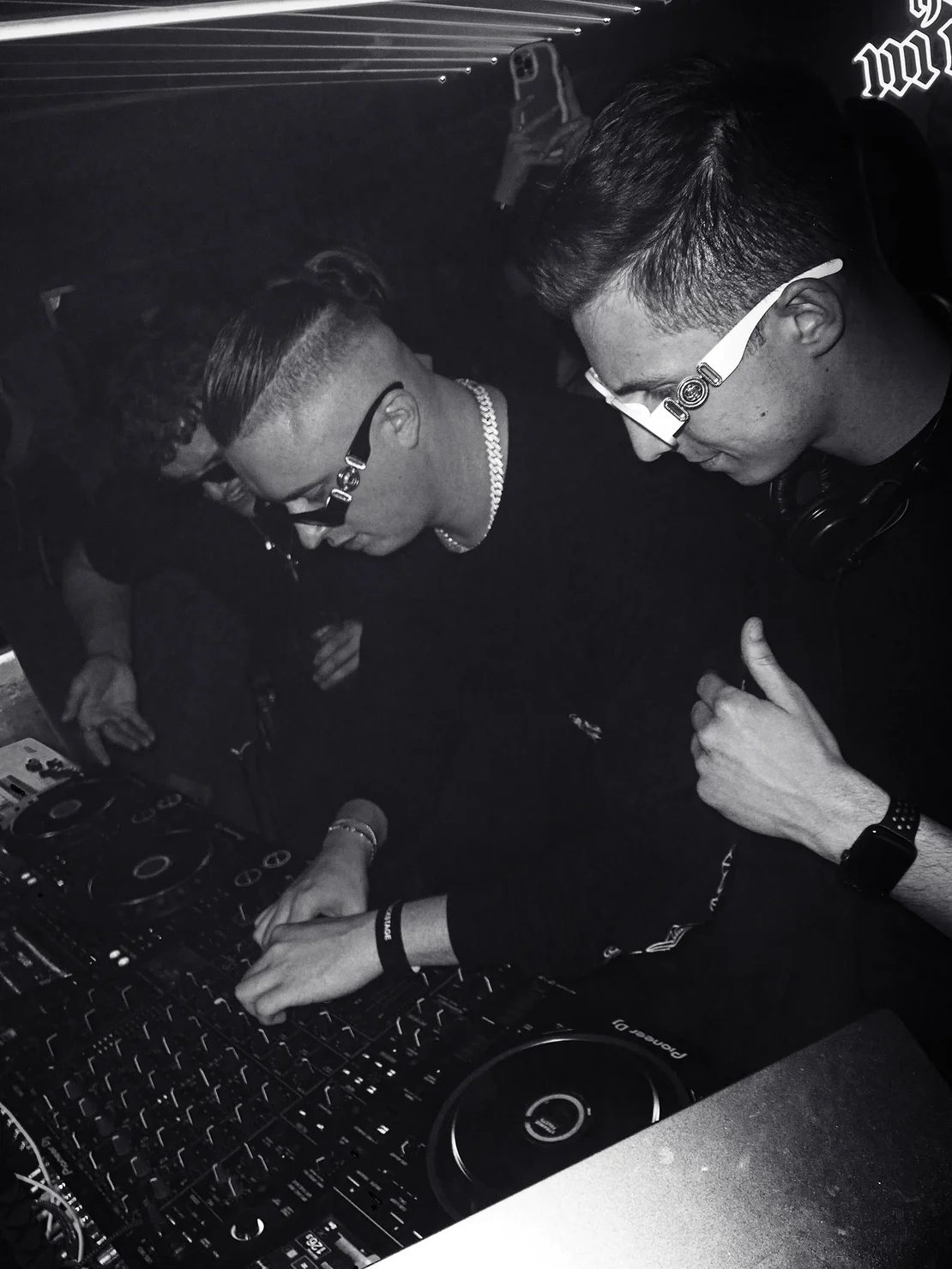 MNEEMO (Yaroslav Gorovoy) & SLAVKO (Viacheslav Zazymko) wearing sunglasses behind the DJ booth in a club. Black-and-white photo, light beams in the background, one of them giving a thumbs-up.