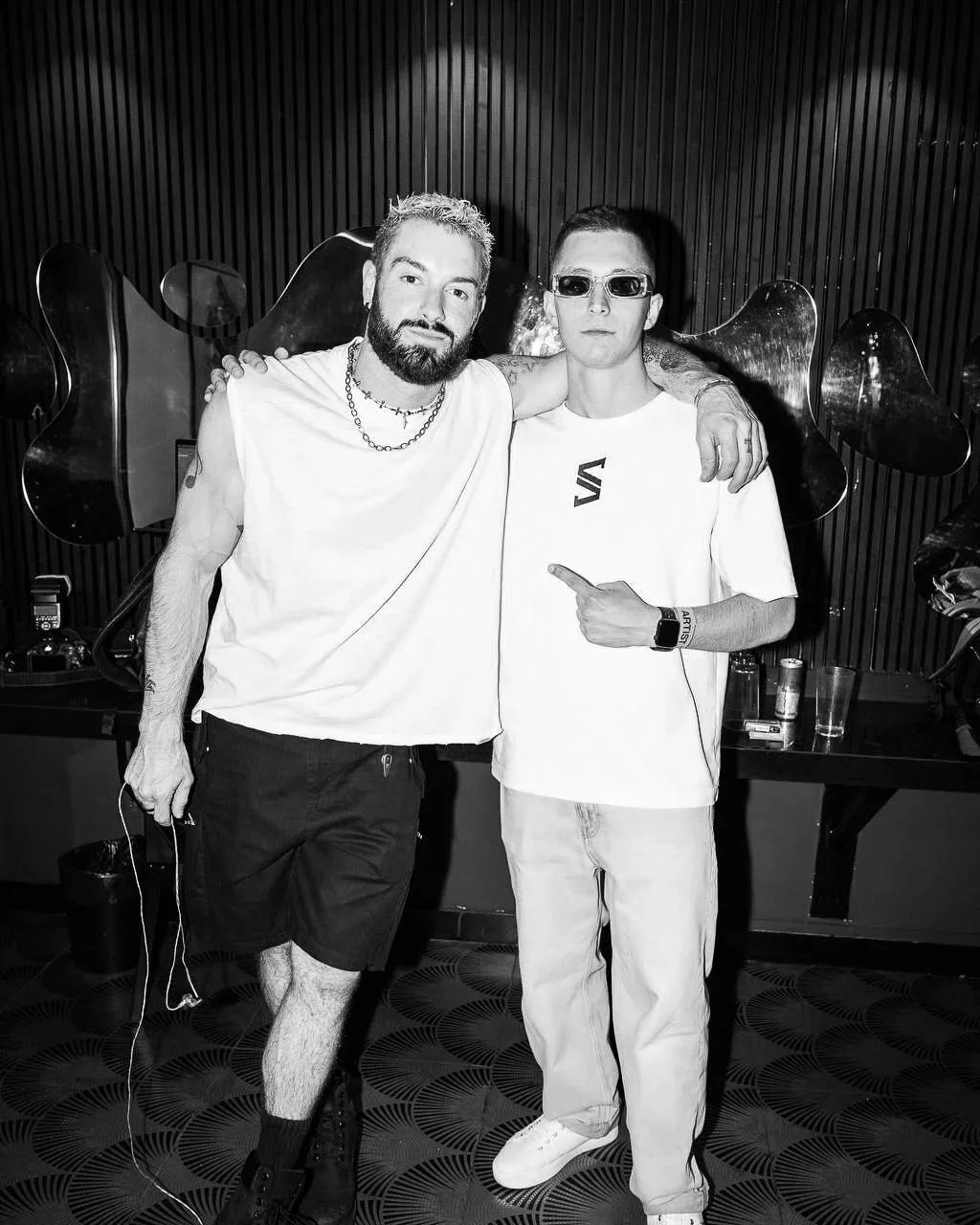 SLAVKO (Viacheslav Zazymko) and James Hype posing in a black-and-white club scene. One is pointing at the other. They are wearing T-shirts, and one of them has glasses on. Friendly mood.