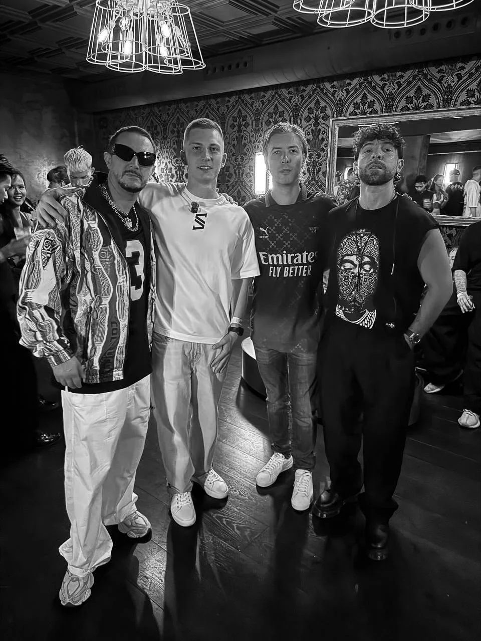 SLAVKO (Viacheslav Zazymko) and MEDUZA (Luca de Gregorio, Mattia Vitale and Simone Giani) standing together indoors with patterned walls. The text “Emirates Fly Better” is visible on the clothing, and everyone appears relaxed.
