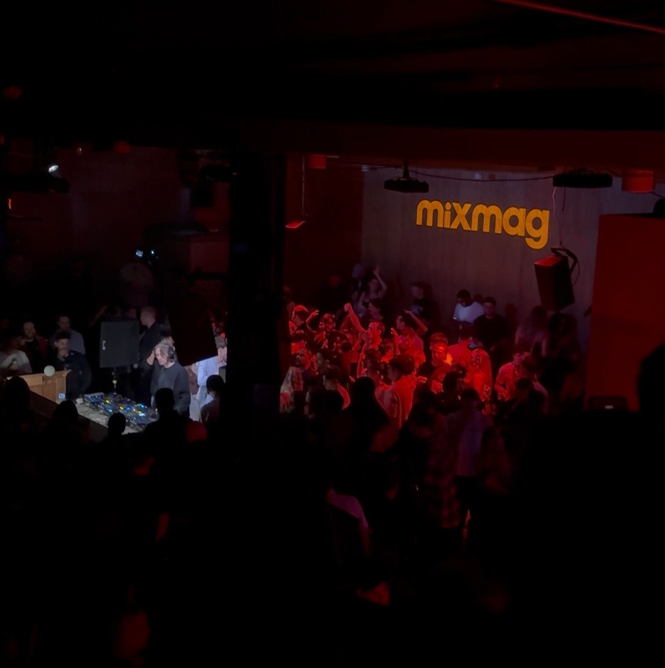 Mixmag Cover Moment for NOTION. a lively crowd in a dimly lit club with red lighting, "mixmag" logo on the wall. Energetic atmosphere.