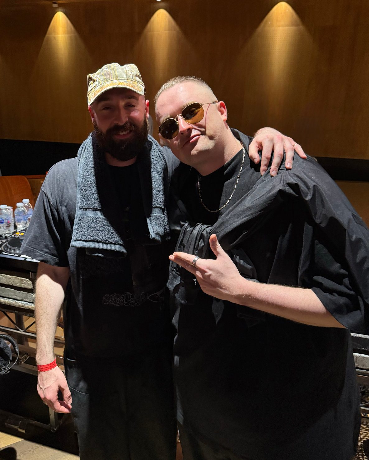 NOTION & MNEEMO (Yaroslav Gorovoy) in black outfits, one with a towel around his neck and the other wearing sunglasses, pose happily under warm lighting indoors during Mixmag Cover Moment.