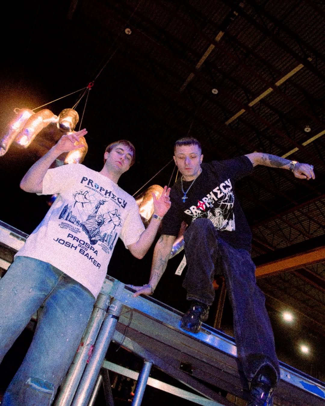 Prospa posing on stage during their PROPHECY live production with industrial lighting and suspended silver hand sculptures.