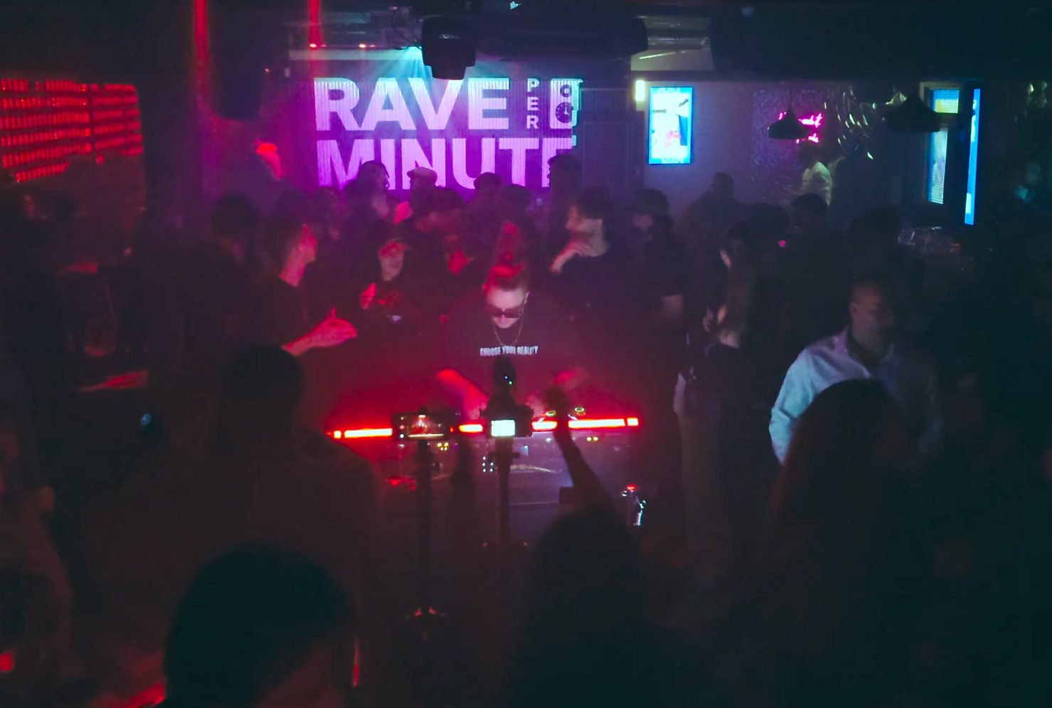 MNEEMO (Yaroslav Gorovoy) wearing glasses, performing on stage with the words “Rave per Minute” displayed behind him. The crowd is dancing in a club with bright lighting effects. Energetic atmosphere.
