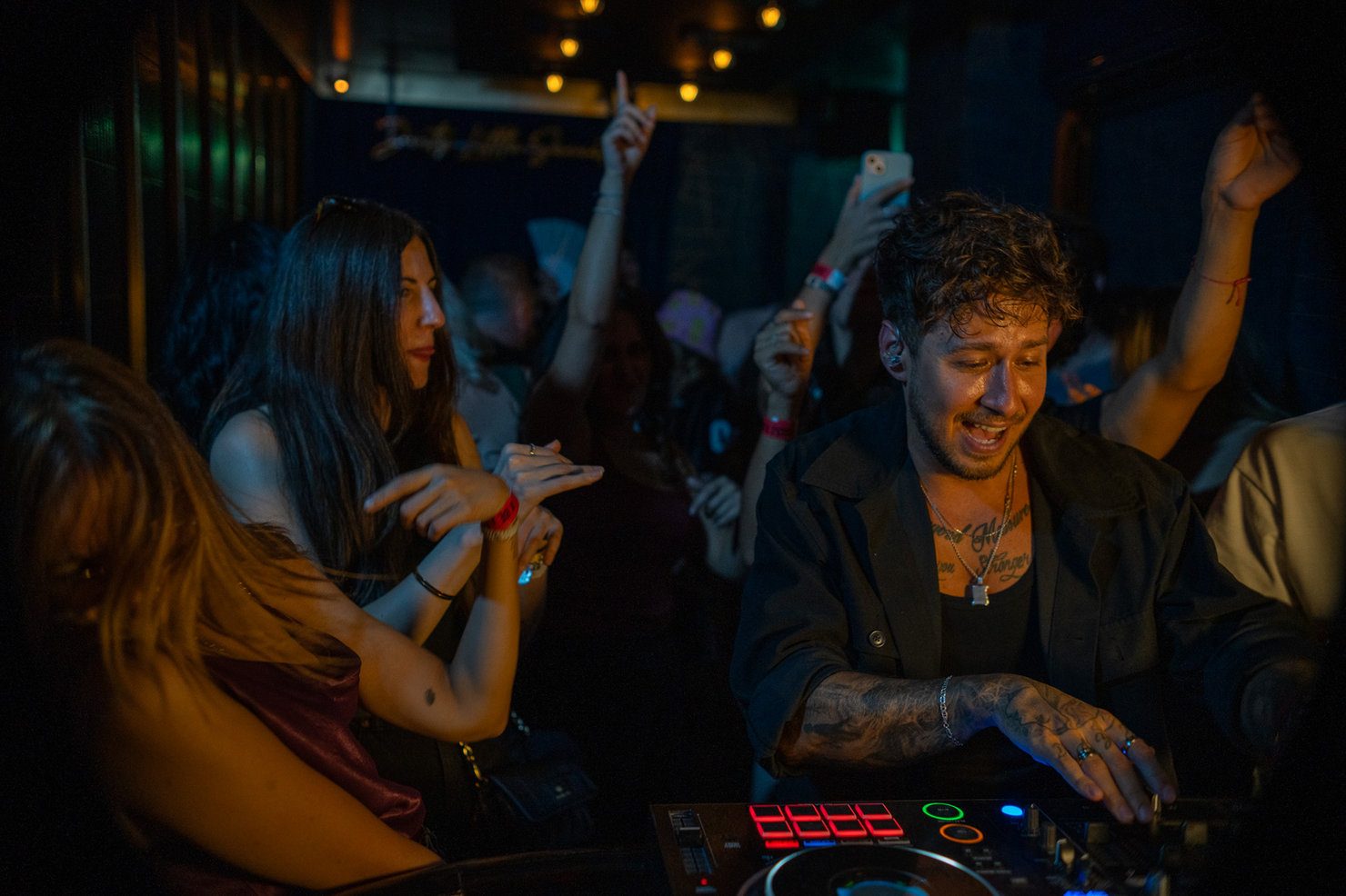 Mike Jasom performing in a club. A crowd is dancing under bright lighting. Joyful atmosphere, with a sign featuring text in the background.