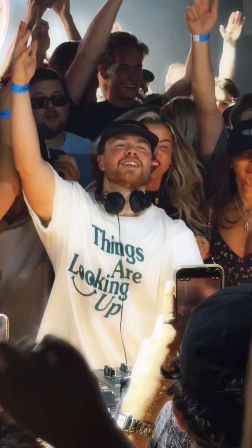 Rossi. smiling with headphones around his neck during his Boiler Room London debut, as the crowd behind him reacts to the set.