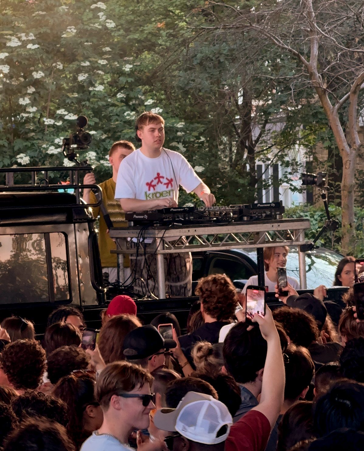 Wide shot of Silva Bumpa performing at the open-air HYPA EP release party in London, with a large crowd gathered under a bridge as daylight and smoke create a raw street-level atmosphere.