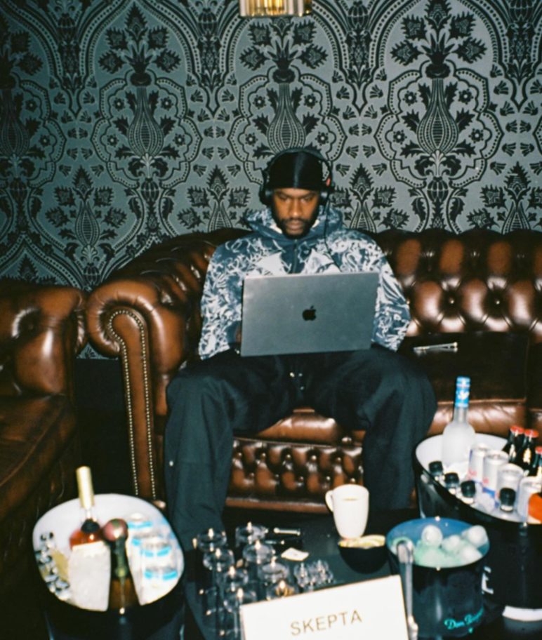 Skepta working on a laptop on a leather sofa, the producer behind the Mas Tiempo Club Room residency